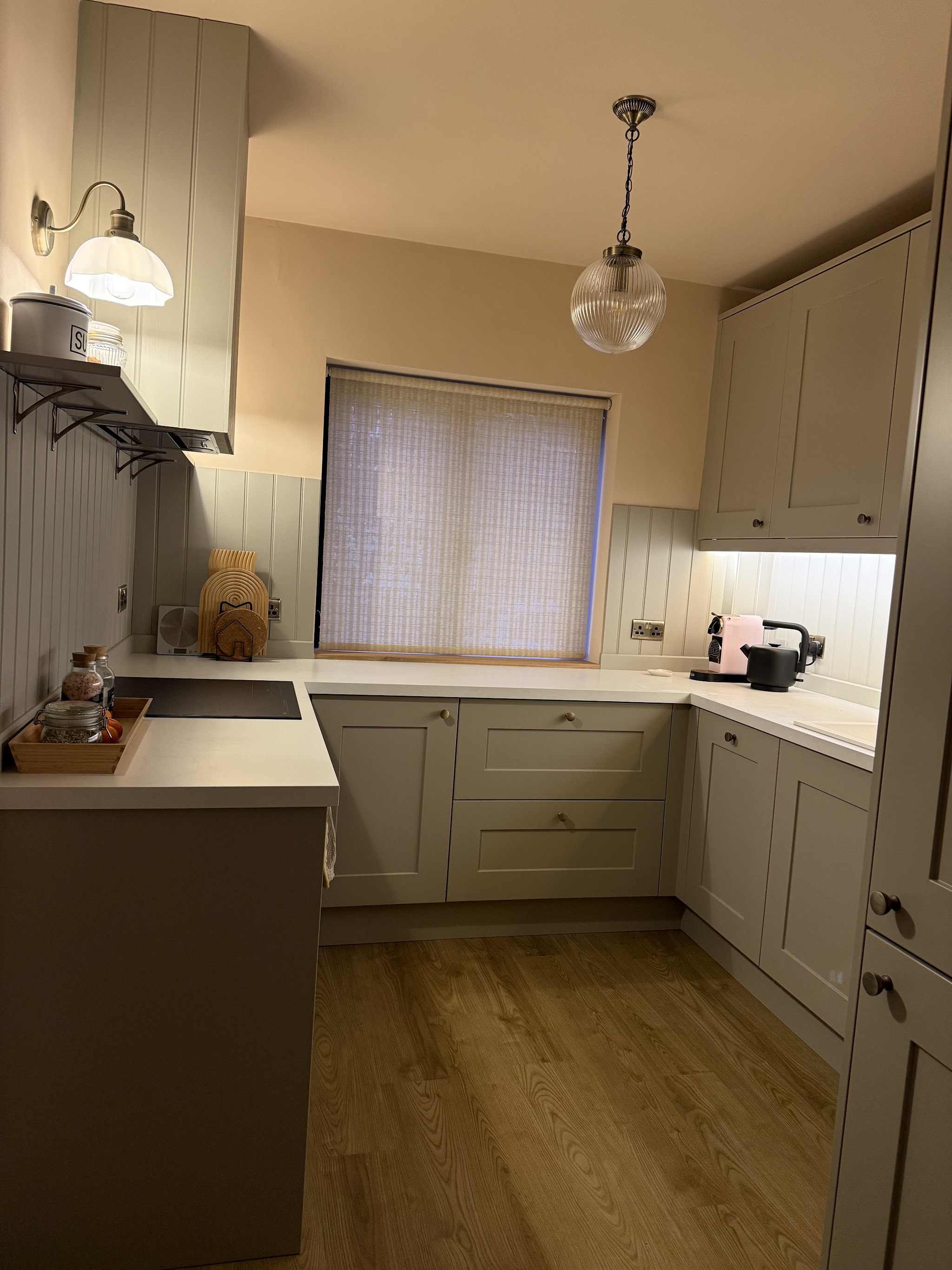 A completed pale fitted kitchen with glass pendant lighting